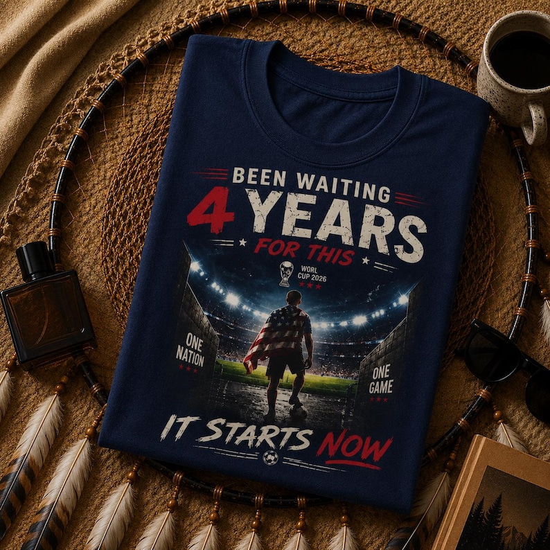 May include: Navy blue t-shirt with the text "Been Waiting 4 Years For This" in red and white. The shirt features a graphic of a soccer player in a stadium with the text "World Cup 2026" and "It Starts Now".
