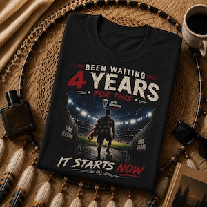 May include: Black t-shirt with a soccer stadium graphic. The shirt features the text "Been Waiting 4 Years For This" in white and red, with "It Starts Now" in red. A soccer ball graphic is at the bottom.