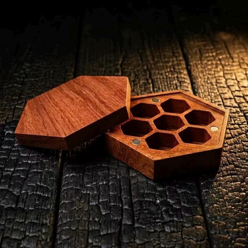 May include: A wooden hexagonal box with a lid, featuring a honeycomb design inside. The box is made of reddish-brown wood and sits on a dark, textured wooden surface. The lid is slightly ajar, revealing the interior compartments.