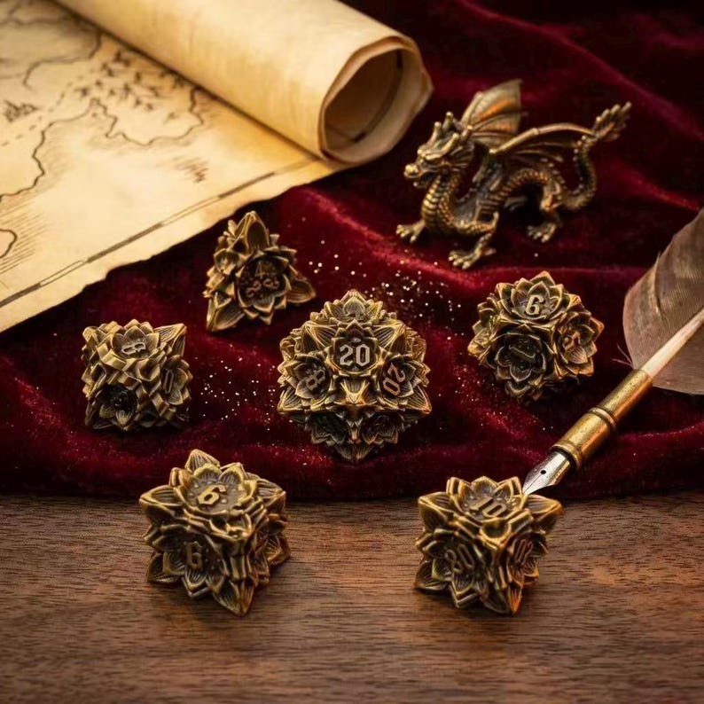 May include: A collection of antique gold-colored polyhedral dice with a floral design, perfect for tabletop games. The set includes a D20, D12, D10, D8, D6, and D4. A small bronze dragon figurine and a scroll are in the background.