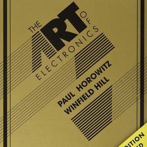 May include: A hardcover book titled The Art of Electronics by Paul Horowitz and Winfield Hill. The cover is tan with black text and diagonal lines. A yellow banner in the bottom right corner reads Third Edition Improved in black text.
