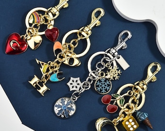 May include: Four metal keychains with lobster clasps and split rings. The first features red hearts, the second has gold letters spelling CAI, the third displays silver snowflake charms, and the fourth includes cherry, dice, and ice cream cone charms.