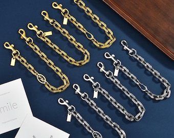 Op de afbeelding: Een collectie metalen portemonneekettingen in goud- en zilverkleur, voorzien van getextureerde ovale schakels, een karabijnsluiting en een klein rechthoekig label. Sommige kettingen bevatten een ovaal bedeltje met een paard-en-wagenmotief.