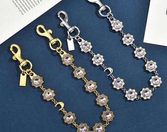 Op de afbeelding: Drie decoratieve kettingen met karabijnsluitingen, elk voorzien van een reeks bloemvormige schakels bezet met lichtpaarse kristallen en kleine witte kralen. Eén ketting is goudkleurig, twee zijn zilverkleurig, allemaal inclusief een kleine maansikkelbedel.