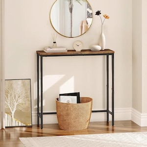 Könnte beinhalten: Ein schmaler Konsolentisch mit einer dunkelbraunen Holzplatte und schwarzen Metallbeinen. Darunter steht ein geflochtener Korb, und darüber hängt ein runder Spiegel. Der Tisch hat ein minimalistisches Design, geeignet für Eingangsbereiche oder Wohnzimmer.