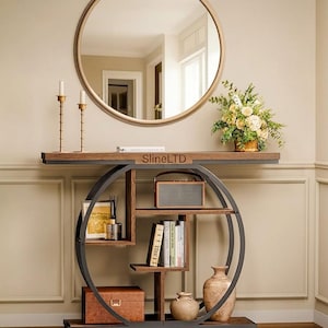 May include: A contemporary console table with a dark metal frame and wooden shelves. The table has a circular design with a shelf for books and decorative items. A round mirror hangs above the table, and a small radio sits on the top shelf.