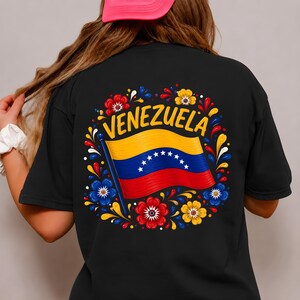 May include: A black t-shirt featuring a graphic on the back with the word VENEZUELA arched over a waving Venezuelan flag. The design is surrounded by a circular arrangement of colorful red, yellow, and blue floral and swirling decorative patterns.