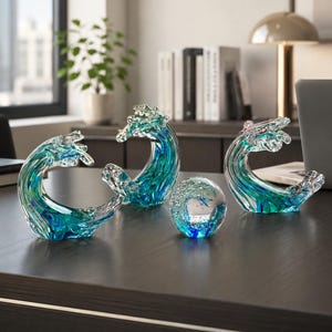 Puede incluir: Tres esculturas de vidrio con forma de olas del oc&eacute;ano y un pisapapeles de vidrio esf&eacute;rico. Cada pieza presenta tonos arremolinados de azul profundo, turquesa y vidrio transparente con burbujas de aire internas, creando un aspecto fluido.