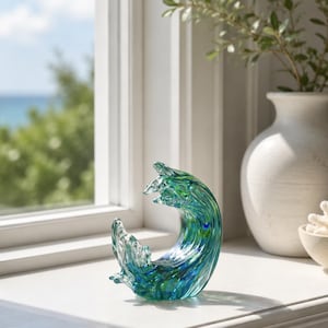 Puede incluir: Una escultura de vidrio con forma de ola oce&aacute;nica, que presenta patrones de remolinos en azul profundo, turquesa y vidrio transparente. La pieza tiene un acabado suave y pulido que captura la luz, creando un efecto transl&uacute;cido que imita el agua.