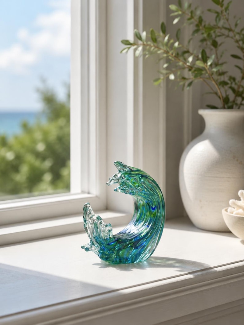 Puede incluir: Una escultura de vidrio con forma de ola oce&aacute;nica, que presenta patrones de remolinos en azul profundo, turquesa y vidrio transparente. La pieza tiene un acabado suave y pulido que captura la luz, creando un efecto transl&uacute;cido que imita el agua.