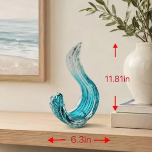Puede incluir: Un adorno de vidrio escultural con una forma fluida similar a una ola en tonos de azul transl&uacute;cido y vidrio transparente. El objeto mide 30 cm de altura y 16 cm de ancho, mostrando una forma curva y org&aacute;nica con detalles texturizados.