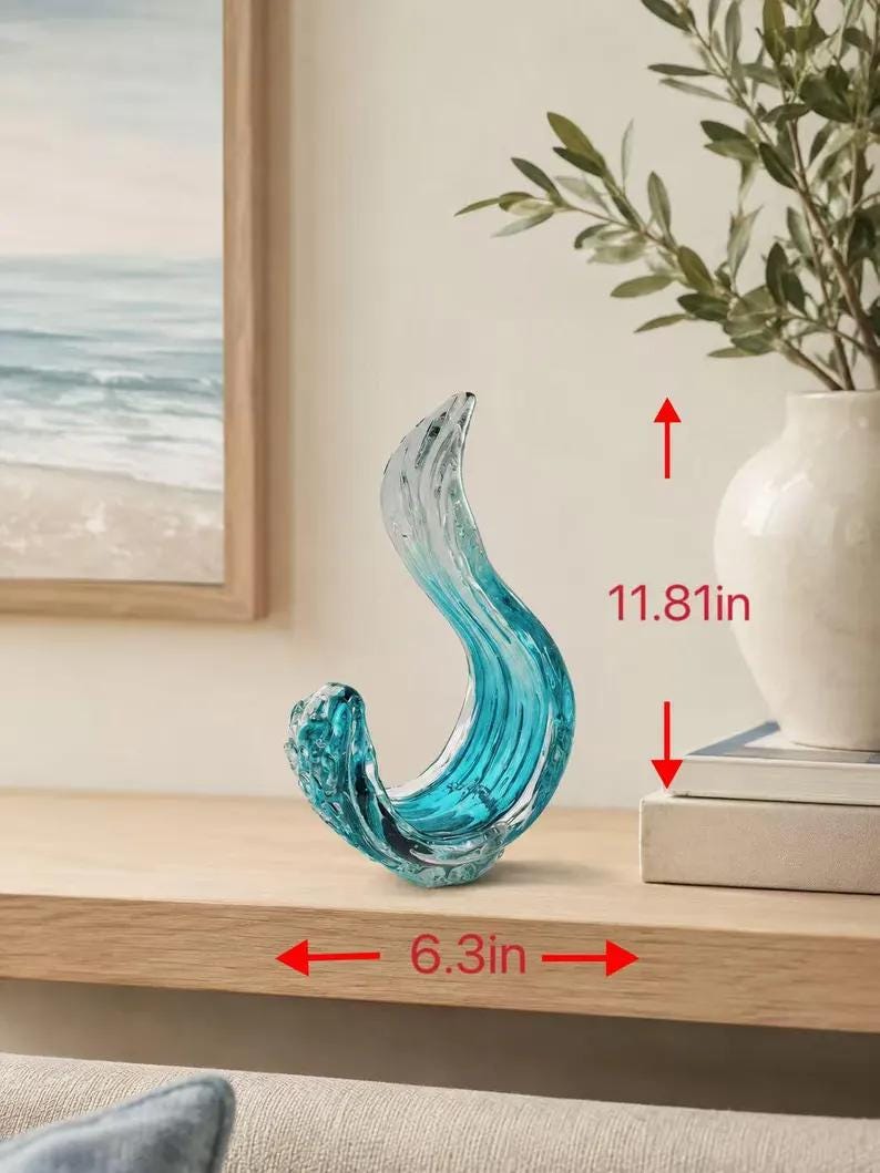 Puede incluir: Un adorno de vidrio escultural con una forma fluida similar a una ola en tonos de azul transl&uacute;cido y vidrio transparente. El objeto mide 30 cm de altura y 16 cm de ancho, mostrando una forma curva y org&aacute;nica con detalles texturizados.
