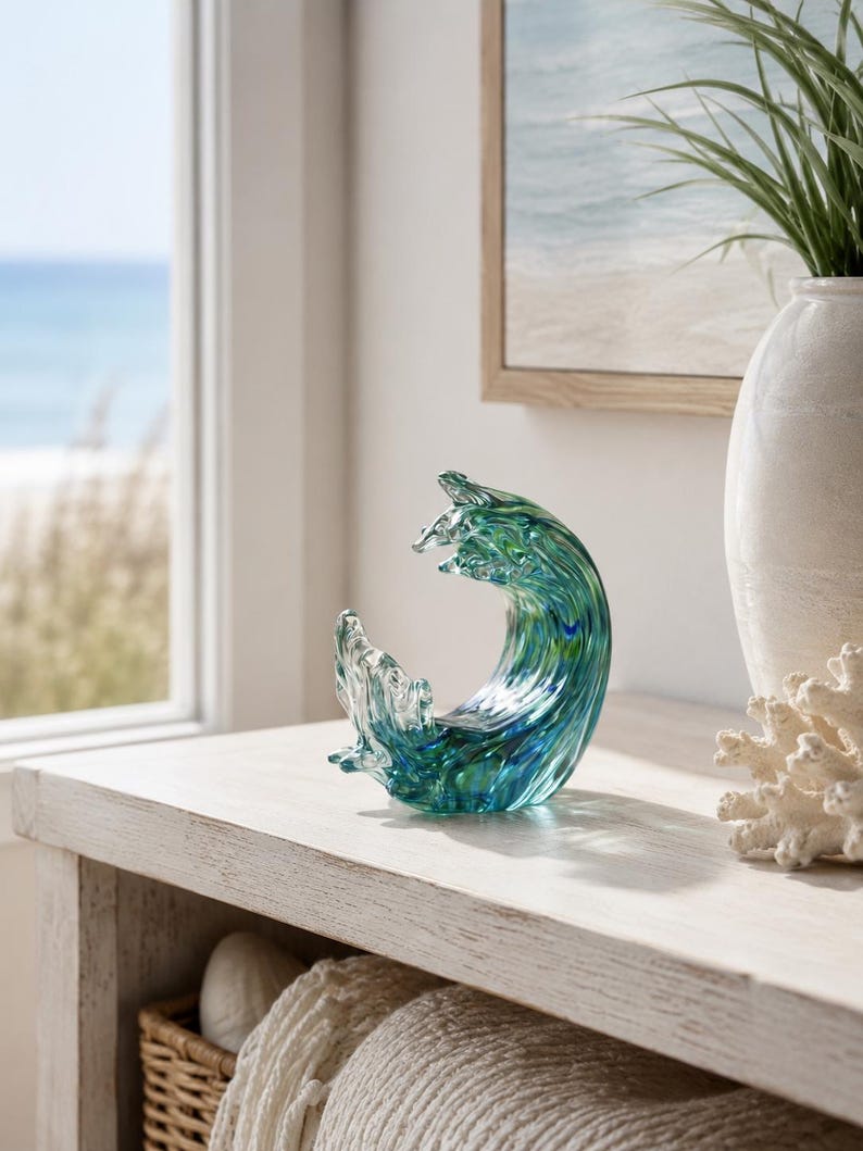 Puede incluir: Una escultura de vidrio con forma de ola oce&aacute;nica, que presenta tonos arremolinados de azul, verde azulado y verde transl&uacute;cidos. La pieza tiene un acabado suave y pulido, capturando el movimiento din&aacute;mico del agua con una cresta superior.