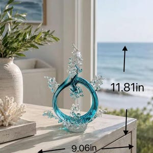 Puede incluir: Una escultura circular de vidrio color verde azulado y transparente con detalles texturizados en forma de olas. La escultura mide 30 cm de alto y 23 cm de ancho, seg&uacute;n lo indicado por las flechas negras y el texto en la imagen.
