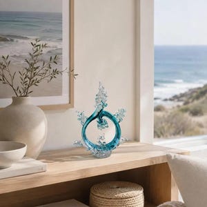 Puede incluir: Una escultura decorativa de cristal con un anillo circular central de color azul cerceta y protuberancias transparentes, dentadas y cristalinas que se extienden hacia arriba y los lados, sobre una base de cristal transparente texturizado.