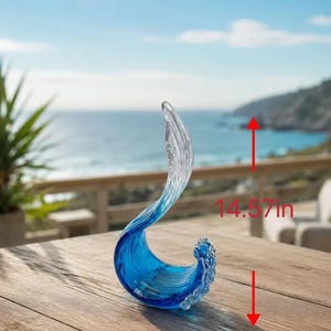 Puede incluir: Una escultura de vidrio transparente y azul con forma de ola rompiendo. La pieza presenta un degradado de azul intenso en la base que se vuelve transparente hacia la parte superior. Una flecha roja indica una altura total de 37 cm.