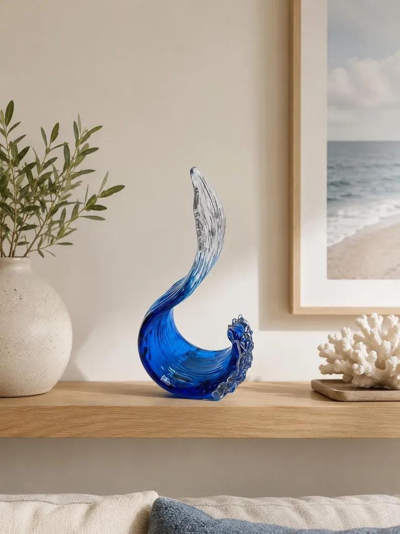 Puede incluir: Una escultura decorativa de vidrio con forma de ola oce&aacute;nica rompiendo, que presenta una base azul intenso que se transforma en una parte superior clara y transl&uacute;cida. La pieza tiene una forma curva y fluida con detalles texturizados.