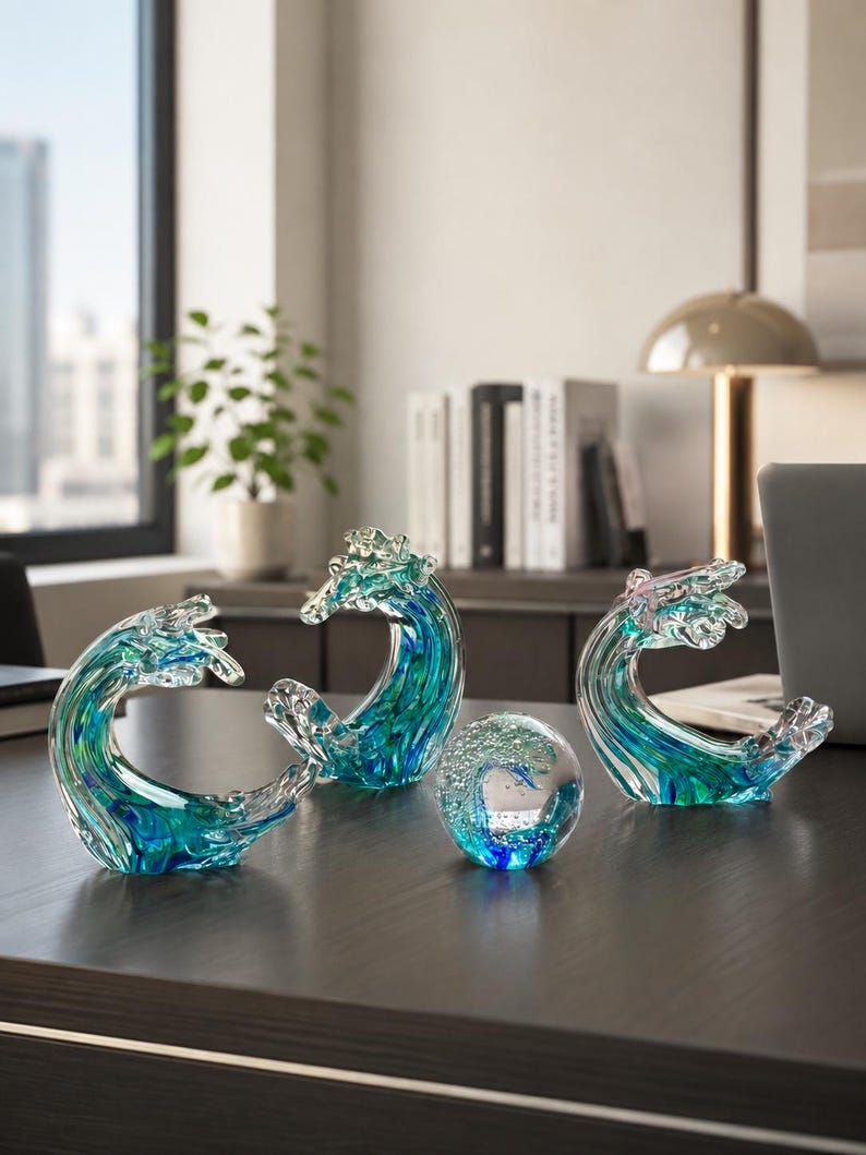 Puede incluir: Tres esculturas de vidrio con forma de olas del oc&eacute;ano y un pisapapeles de vidrio esf&eacute;rico. Cada pieza presenta tonos arremolinados de azul profundo, turquesa y vidrio transparente con burbujas de aire internas, creando un aspecto fluido.