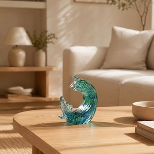 Puede incluir: Una escultura decorativa de cristal con forma de ola oce&aacute;nica, que presenta tonos transl&uacute;cidos de azul profundo, turquesa y verde. La pieza tiene un acabado liso y pulido con patrones de color en espiral que imitan el movimiento del agua.