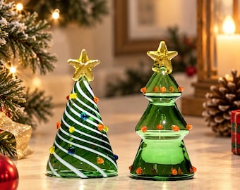 May include: Two glass Christmas tree figurines. The left tree is green with white diagonal stripes and small colorful glass dots. The right tree is a tiered green glass shape with small orange dots. Both trees are topped with a yellow star.