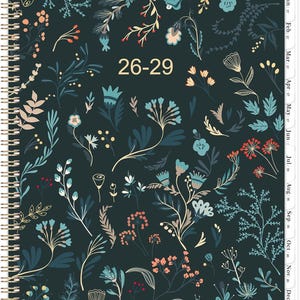 May include: A spiral-bound planner with a dark teal cover adorned with a floral pattern in shades of blue, peach, and white. The text "26-29" is visible. The planner includes monthly tabs and dates from January to December.