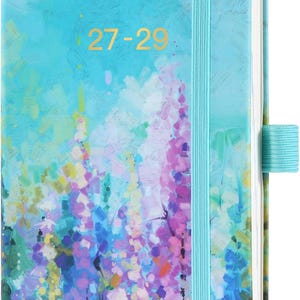 May include: A rectangular planner with a hard cover featuring an impressionistic floral print in shades of blue, purple, yellow, and green. The text 27-29 is printed in gold on the front. It includes a light blue elastic closure and pen loop.