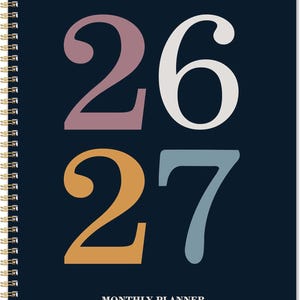 May include: A spiral-bound monthly planner with a navy blue cover. The numbers "26" are in mauve and white, and "27" are in orange and blue. The text "MONTHLY PLANNER" is at the bottom in white.