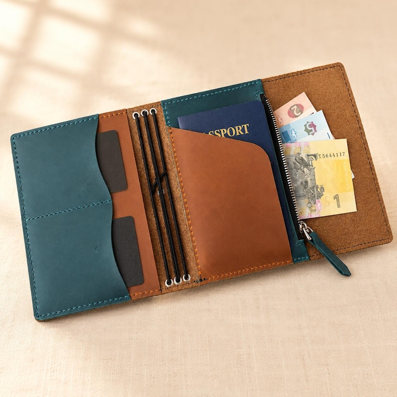 Pode incluir: Uma carteira de viagem de couro multicolorida com pain&eacute;is em azul-petr&oacute;leo e marrom, tr&ecirc;s cord&otilde;es el&aacute;sticos pretos para prender encartes, um compartimento para passaporte, um bolso com z&iacute;per e v&aacute;rias divis&oacute;rias para cart&otilde;es com notas.
