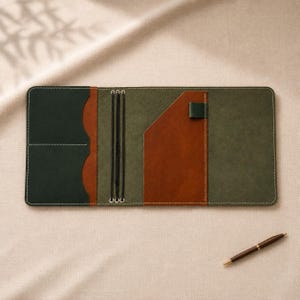May include: A rectangular leather notebook cover featuring a tri-colour design in dark green, olive green, and tan brown. The interior includes multiple card slots, a vertical pocket, a pen loop, and three elastic bands for securing notebook inserts.
