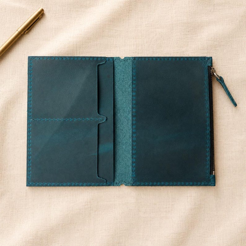 May include: A teal leather passport holder or wallet featuring two card slots on the left side and a zippered compartment on the right side. The interior is constructed with visible stitching along the edges and a matching teal leather pull tab.