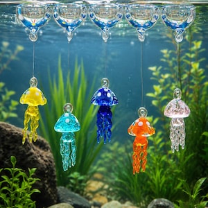 May include: Five glass jellyfish ornaments in yellow, turquoise, blue, orange, and pink, each featuring white spots on the bell and dangling tentacles. The ornaments are suspended by thin wires from clear glass floats at the water surface.