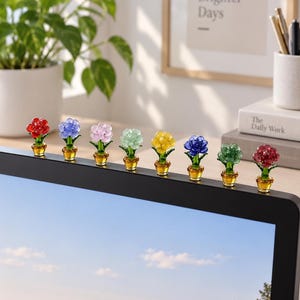 May include: A row of eight miniature glass flower figurines in various colors, including red, blue, pink, light green, yellow, dark blue, and dark green, each set in a small amber-colored glass pot, perched along the top edge of a computer monitor.