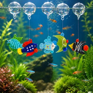 May include: Five colorful glass fish ornaments hang from clear glass spheres floating on a horizontal line. The fish are crafted in various shapes and colors, including blue, green, yellow, red, and black and white stripes, suspended by thin strings.