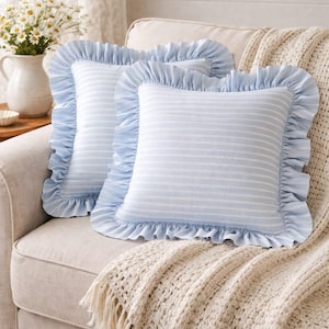 May include: Two square throw cushions featuring a light blue and white horizontal striped pattern. Each cushion is finished with a wide, gathered ruffle border in the same light blue fabric, creating a soft, decorative edge around the entire perimeter.