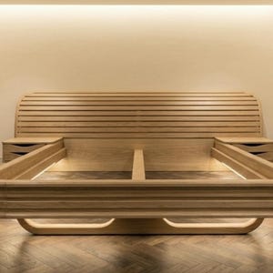May include: A contemporary wooden bed frame featuring a slatted headboard and integrated bedside tables. The bed frame has a curved design with a layered base. The bed frame is made of light-coloured wood and is set against a neutral background.