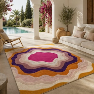 Puede incluir: Una alfombra colorida con un diseño abstracto en capas. La alfombra presenta un centro fucsia vibrante, rodeado de anillos concéntricos de color naranja, morado, rosa y crema. La alfombra es rectangular y está colocada en un patio.