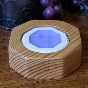 May include: A wooden, octagonal coaster with a light blue, geometric center. The coaster is made of light-colored wood with visible grain. The center is a white octagon with a light blue, geometric shape in the middle.
