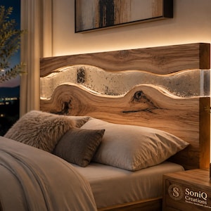 Puede incluir: Un cabecero de madera rectangular con un diseño natural de borde vivo y una incrustación horizontal de resina translúcida en el centro. El cabecero está iluminado por una luz LED cálida integrada que resalta la veta de la madera.