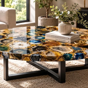 May include: A round coffee table with a unique agate stone top in shades of blue, gold, and brown. The table has a black metal base and is placed on a beige rug. Decorative items are on the table.