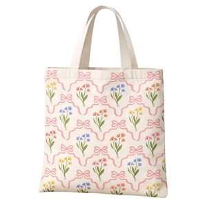May include: A cream-colored tote bag with a repeating floral pattern. The pattern features bouquets of yellow, pink, and blue flowers, connected by pink ribbons and bows. The bag has two cream-colored handles.