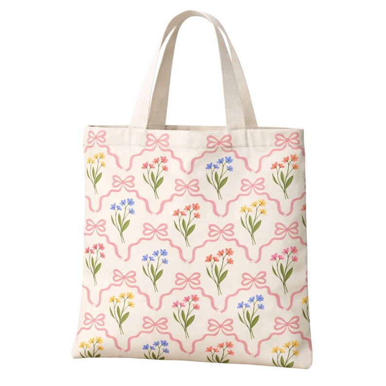 May include: A cream-colored tote bag with a repeating floral pattern. The pattern features bouquets of yellow, pink, and blue flowers, connected by pink ribbons and bows. The bag has two cream-colored handles.