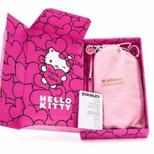 May include: A bright pink gift box featuring a repeating heart pattern and a Hello Kitty graphic holding a heart. Inside, a light pink drawstring pouch with the Stanley and LoveShackFancy logos sits next to a white Stanley care and use instruction card.