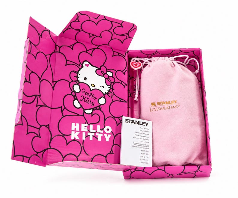 May include: A bright pink gift box featuring a repeating heart pattern and a Hello Kitty graphic holding a heart. Inside, a light pink drawstring pouch with the Stanley and LoveShackFancy logos sits next to a white Stanley care and use instruction card.