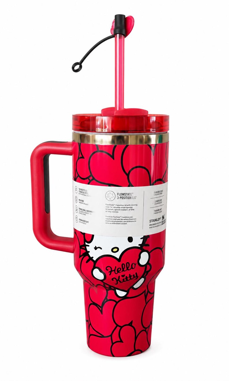 May include: A red stainless steel tumbler featuring a repeating black heart pattern and a Hello Kitty graphic holding a heart. It includes a red handle, a clear lid with a red straw, and a white product label detailing the FlowState 3-position lid.