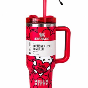 May include: A red Stanley Quencher H2.0 tumbler with a 40 oz capacity, featuring a Hello Kitty graphic, a heart-patterned exterior, a red handle, a clear lid, and a red straw topped with a heart-shaped accessory. The label displays the text Stanley.