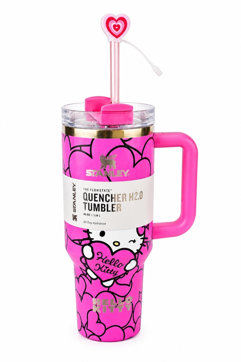 May include: A bright pink 40 oz Stanley Quencher H2.0 tumbler featuring a Hello Kitty graphic, black heart outlines, and a gold rim. The cup includes a pink handle, a clear lid, and a straw topped with a pink and white heart-shaped accessory.