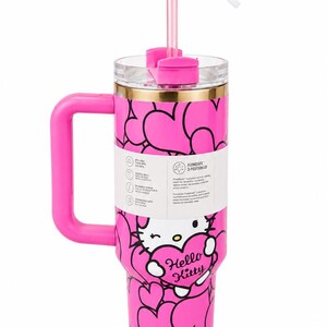 May include: A bright pink insulated tumbler featuring a repeating heart pattern and a Hello Kitty graphic. The cup includes a pink handle, a clear lid with a 3-position FlowState mechanism, and a pink straw topped with a heart-shaped charm.
