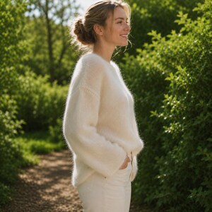 May include: A long-sleeved, cream-colored knit sweater with a fuzzy, soft texture and a round neckline. The sweater features a relaxed fit with dropped shoulders and is paired with matching cream-colored pants, creating a monochromatic look.