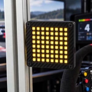 Peut inclure: Un panneau d'affichage LED carré doté d'un cadre à texture fibre de carbone avec quatre vis aux coins. L'appareil contient une grille de huit par huit, soit soixante-quatre carrés lumineux jaunes, monté sur un profilé d'extrusion en aluminium argenté.