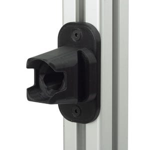 Puede incluir: Un soporte de montaje negro impreso en 3D con una extensión hueca de forma rectangular y una placa base plana. El soporte está fijado a un perfil de extrusión de aluminio plateado vertical mediante dos tornillos hexagonales negros.